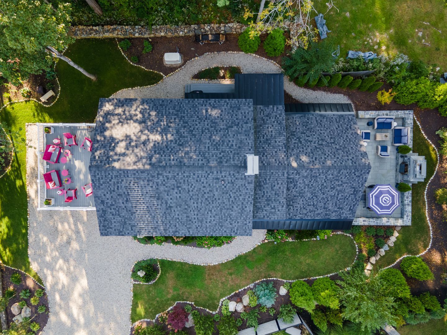 Aerial view of a house with a gray roof, stone patio, driveway, and landscaped garden.