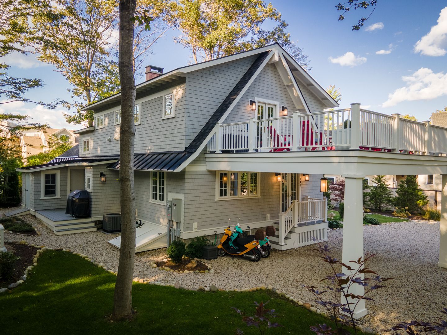 Two-story house with white balcony and deck, surrounded by trees and a gravel yard at dusk