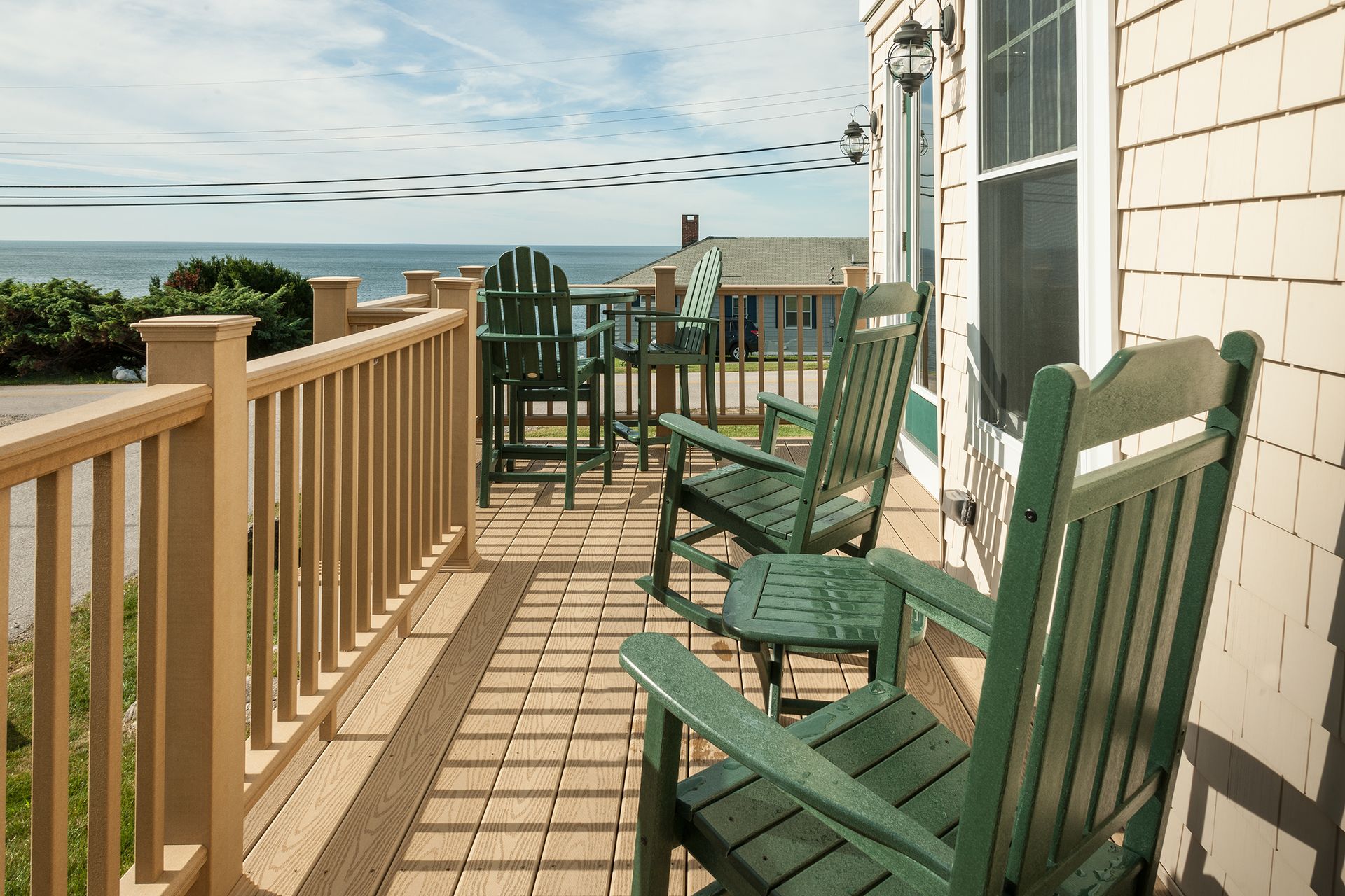 Green rocking chairs on a sunlit beach house porch with ocean view