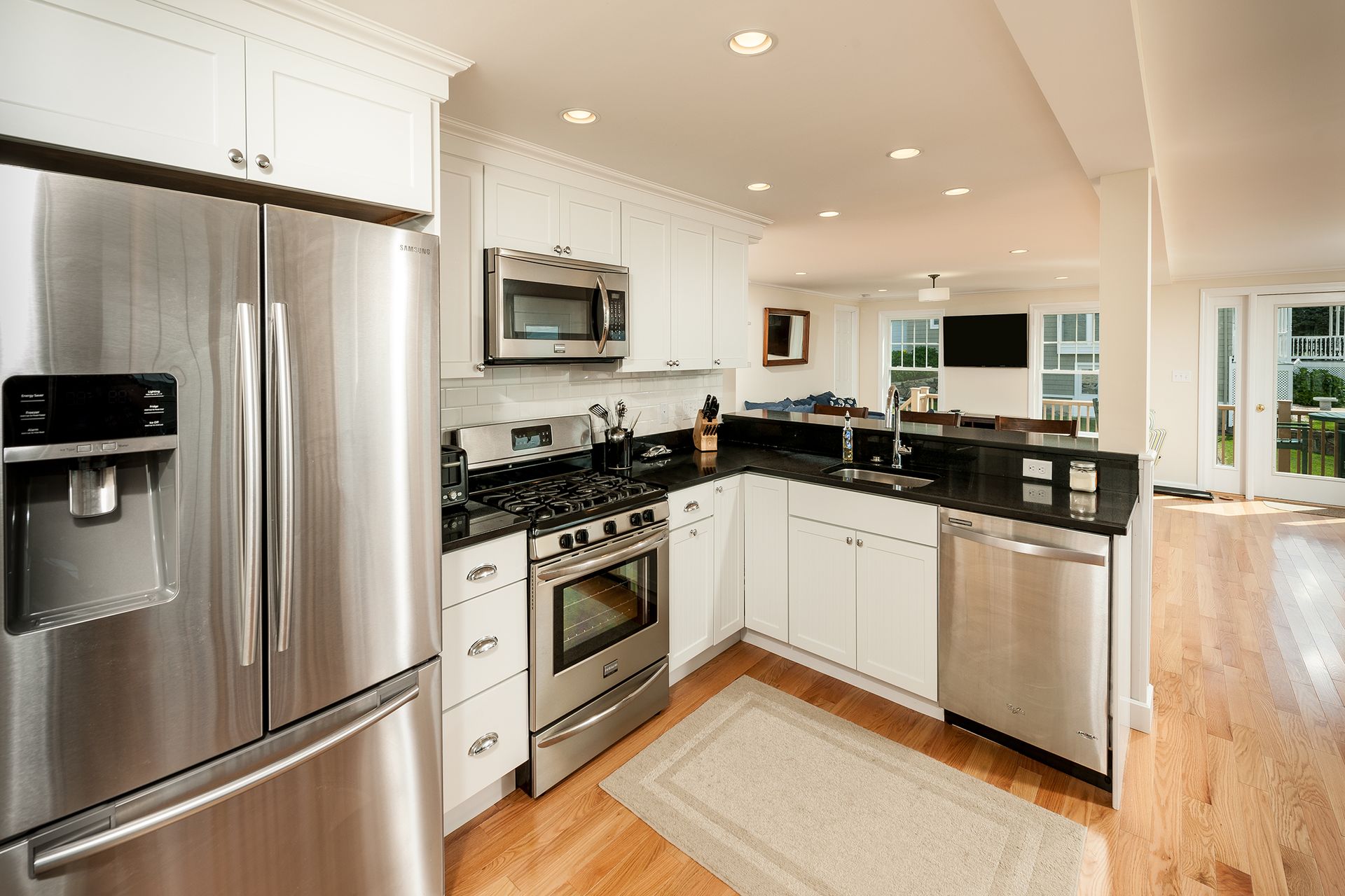 Bright modern white kitchen with stainless steel appliances, black countertops, and hardwood floors