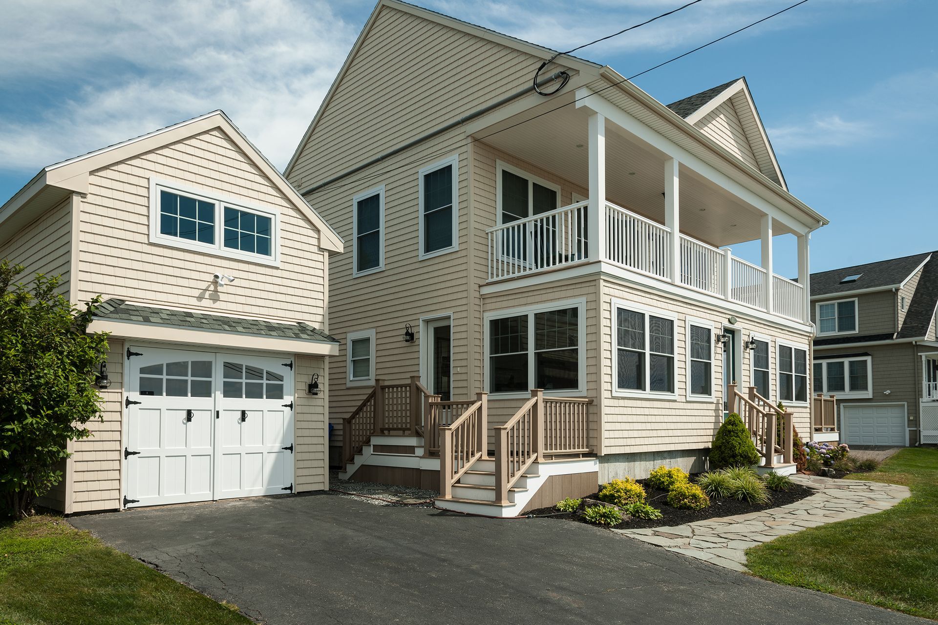 Two-story beige house with white trim, porch, and detached garage on a paved driveway