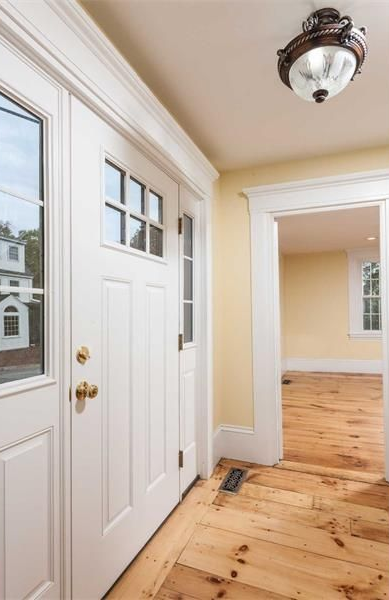 Front entryway with white doors, wood floors, and beige walls leading to a bright room.