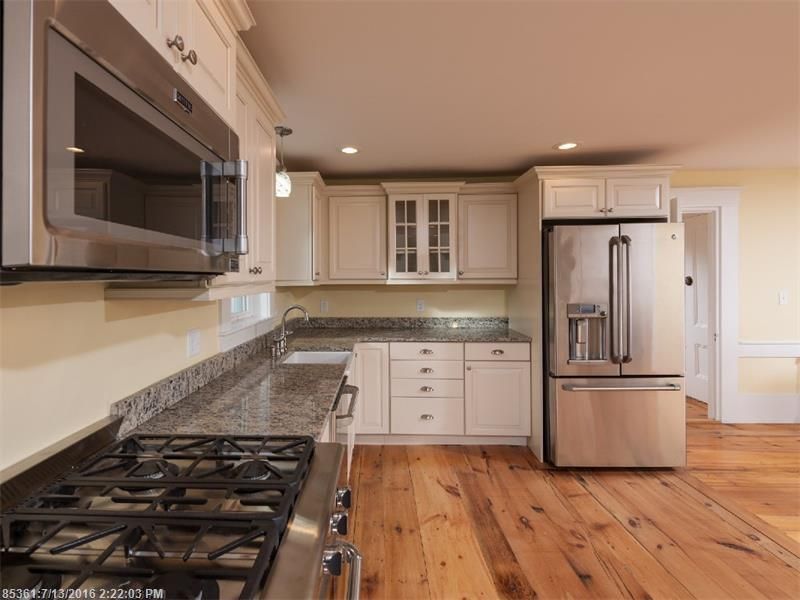 Modern kitchen with stainless steel appliances, white cabinets, granite counters, and hardwood floors