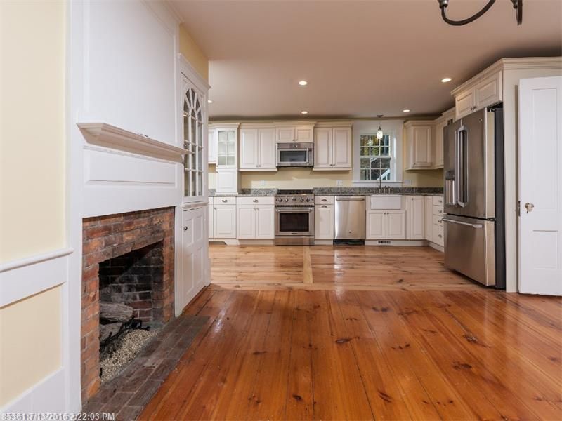 Bright kitchen with white cabinets, stainless appliances, wood floors, and a brick fireplace in the foreground