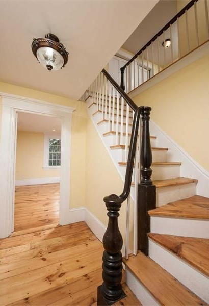 Interior hallway with wooden stairs, black banister, and light yellow walls