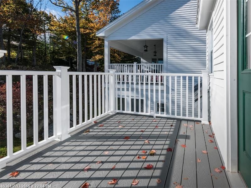 White-railed porch with gray deck boards and a green door, lit by sunlight with scattered autumn leaves