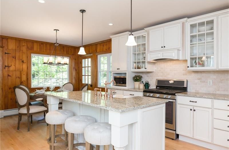 Bright kitchen with white cabinets, granite island, bar stools, and wood-paneled dining nook.