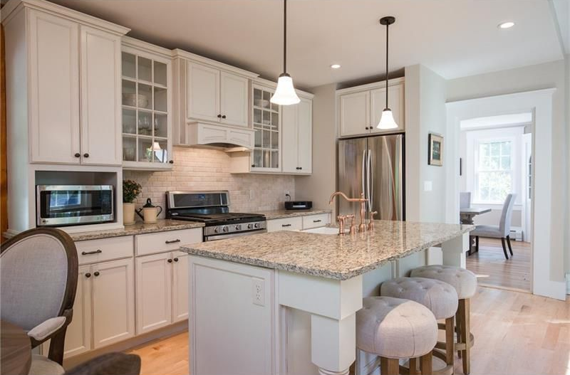 Bright modern kitchen with white cabinets, granite island, stainless steel fridge, and pendant lights
