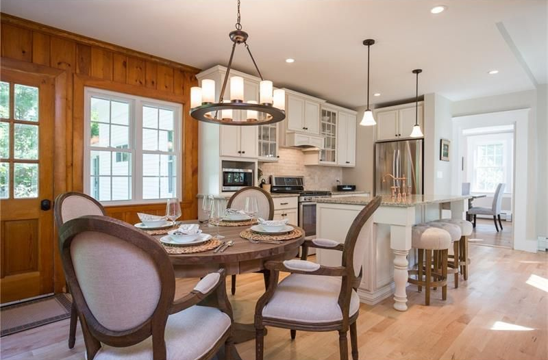 Bright kitchen and dining area with round table, upholstered chairs, white cabinets, and island stools