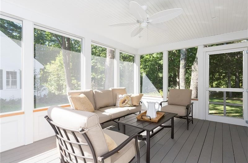 Bright screened porch with beige seating, a coffee table, and large windows overlooking a green yard
