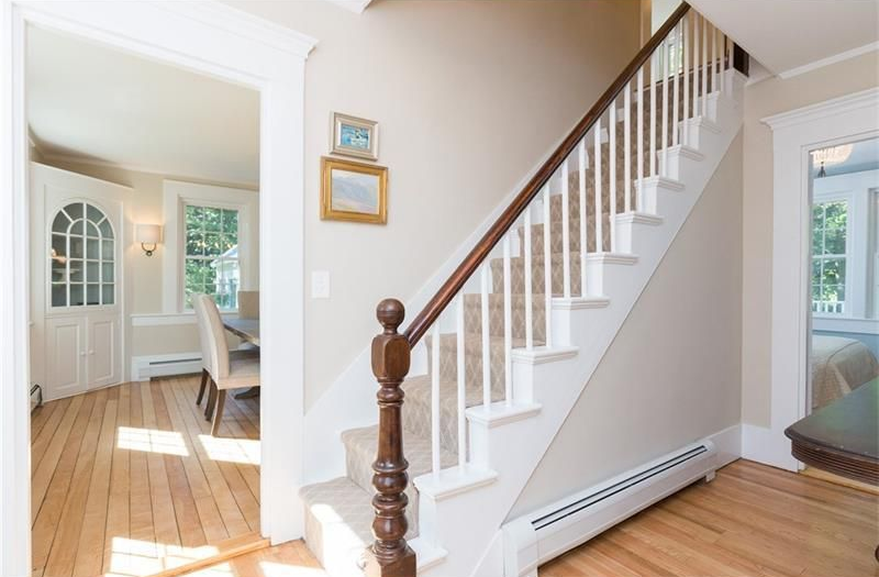 Bright foyer with white staircase, hardwood floors, and doorway into a dining room