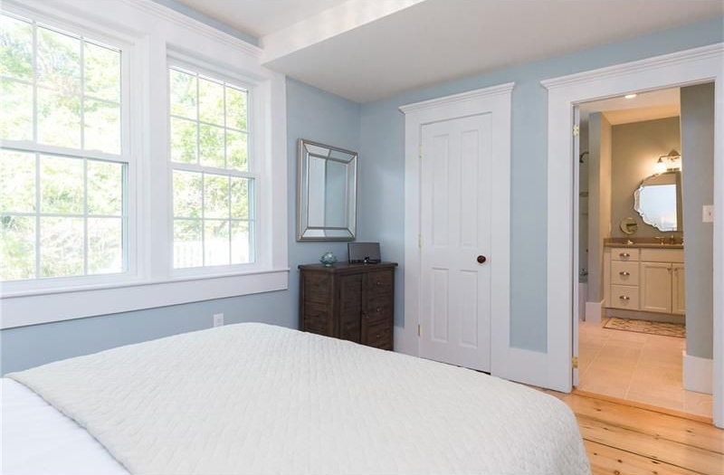 Bright bedroom with light blue walls, white bed, and a doorway to a bathroom.