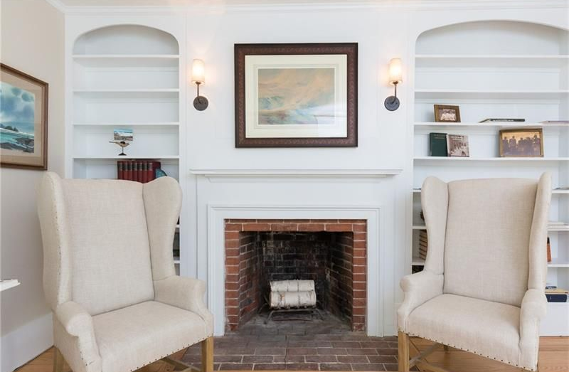 Bright living room with two cream armchairs facing a white fireplace and built-in shelves