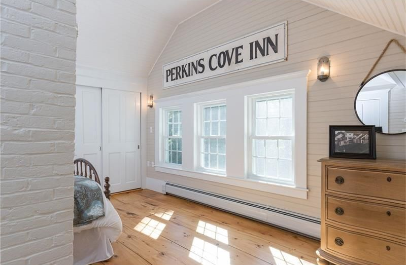 Bright inn room with white walls, wood floor, windows, and a “Perkins Cove Inn” sign above the bed area