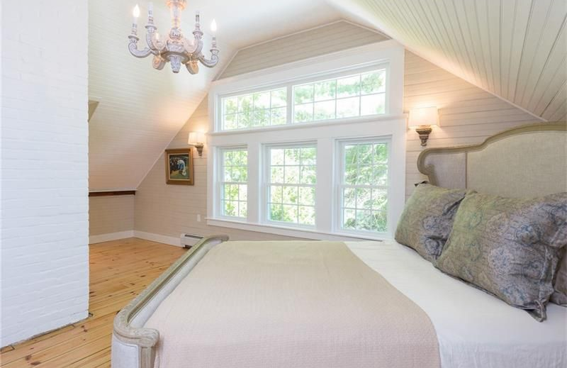 Bright bedroom with white walls, large windows, and a bed with gray pillows in the foreground