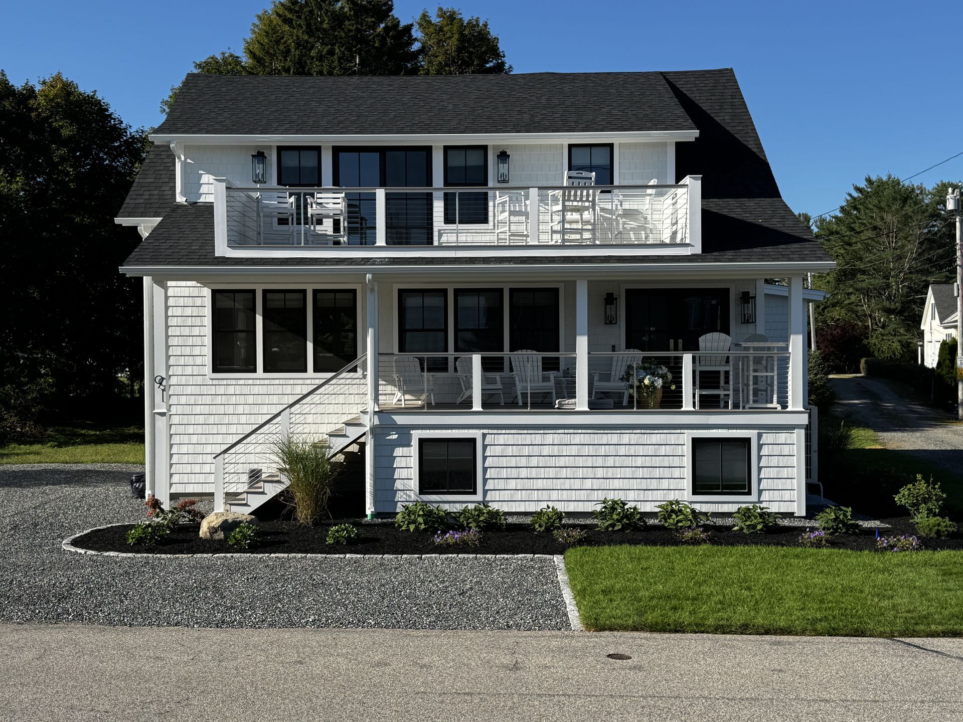 Two-story white house with balcony, dark roof, and front porch on a sunny street
