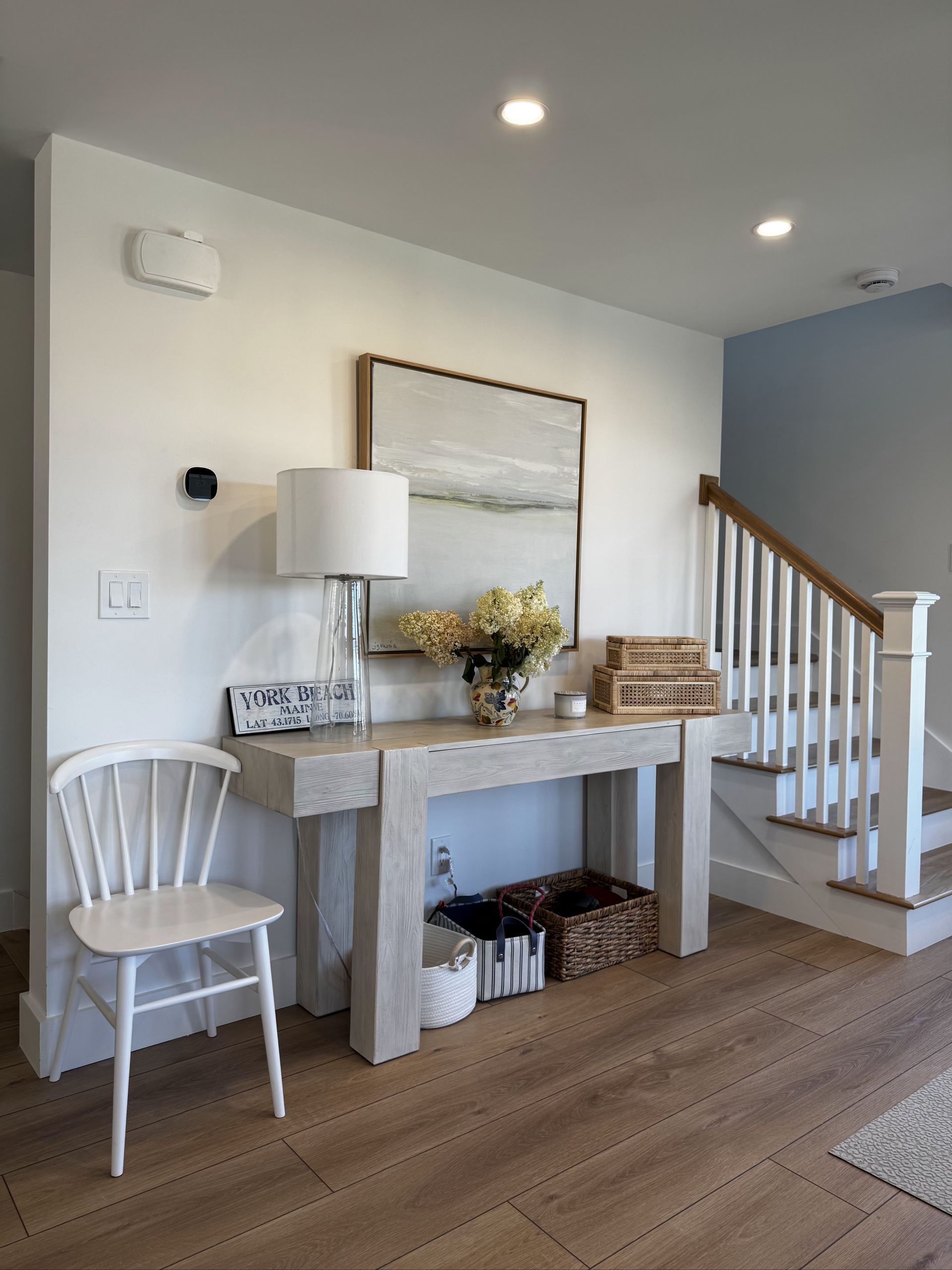 Bright entryway with console table, chair, lamp, wall art, and staircase with wooden railing