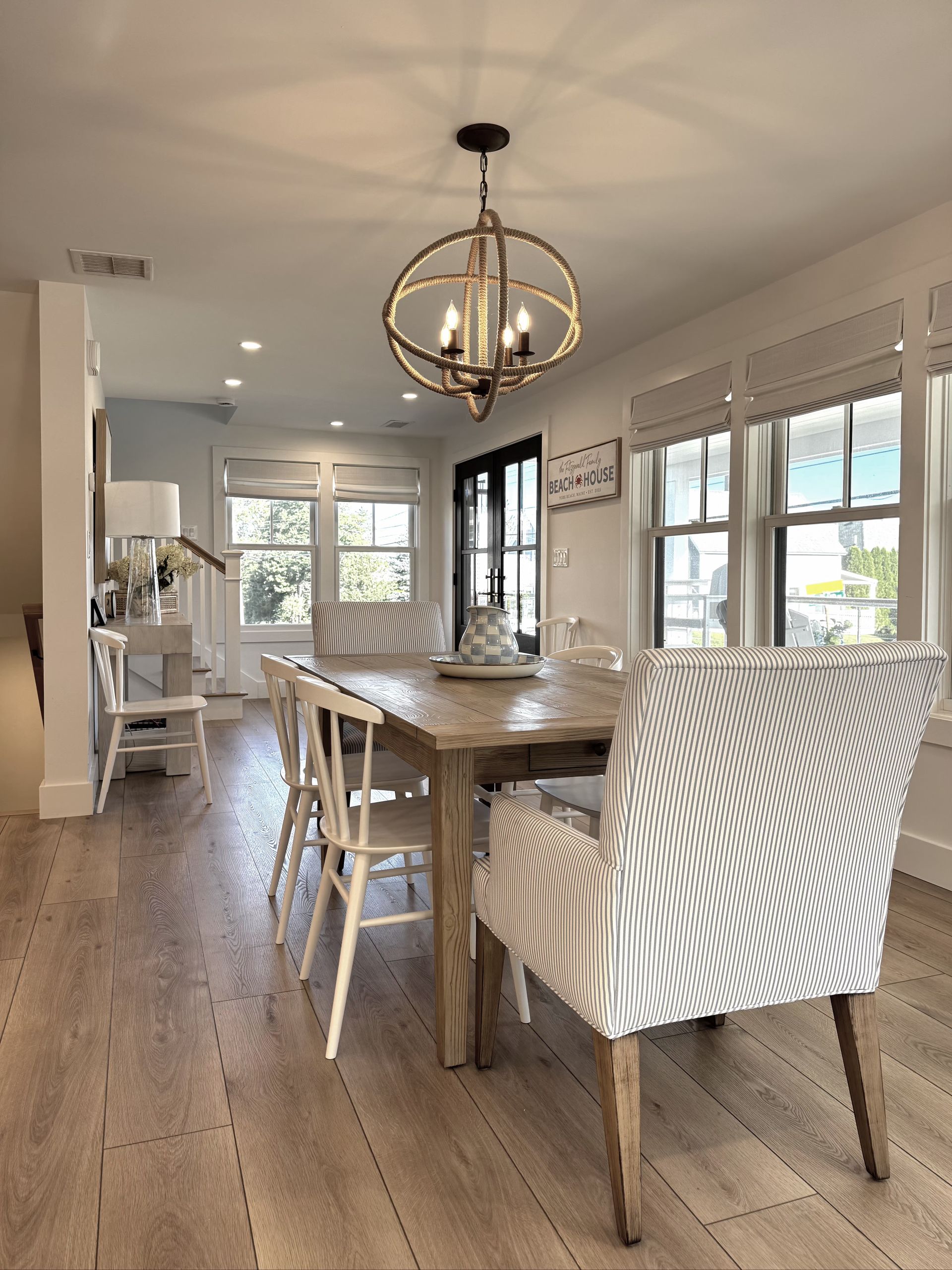 Bright dining room with a wooden table, white chairs, pendant light, and large windows.