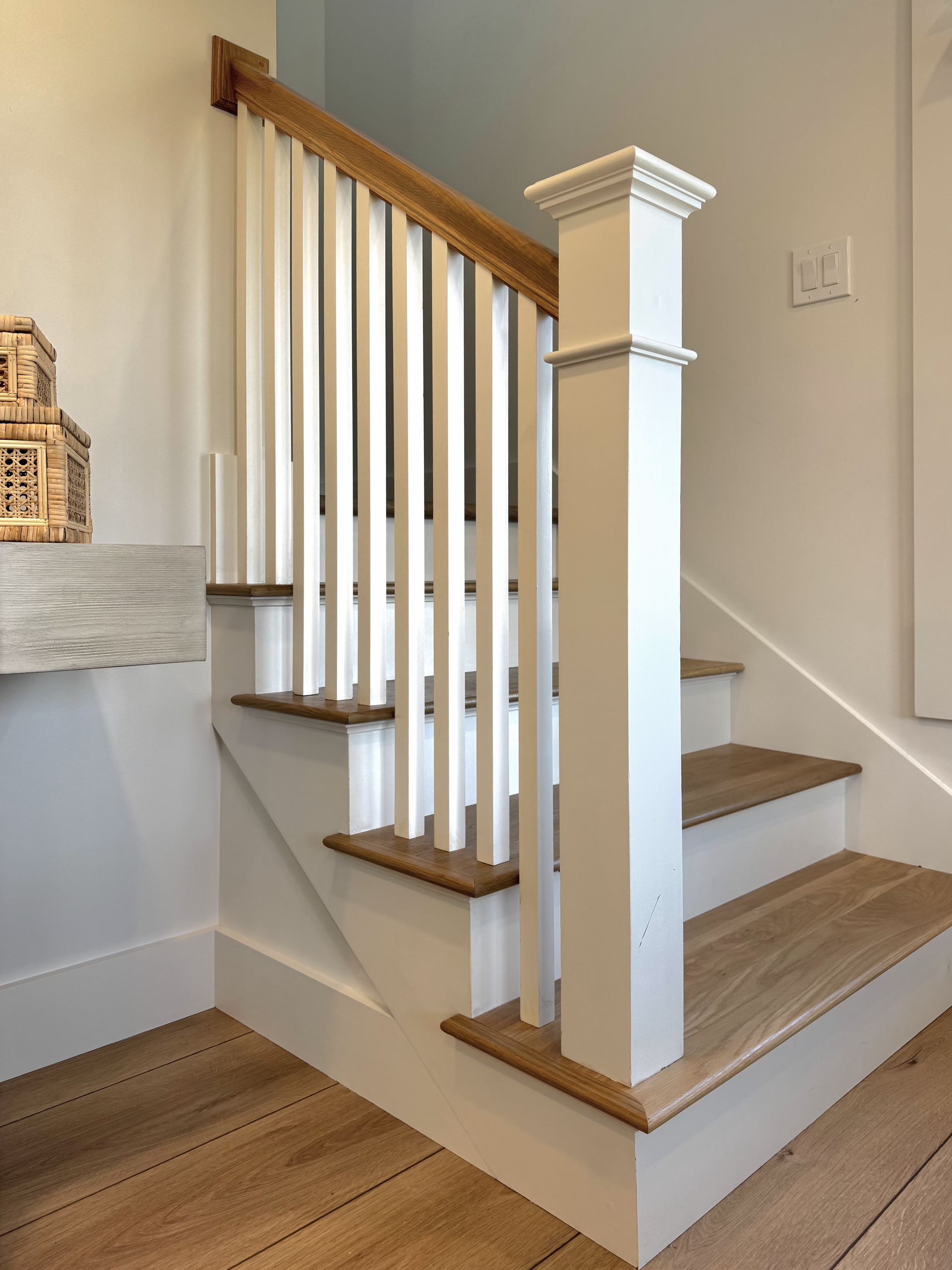 Staircase with wood treads, white balusters, and a white newel post in a bright interior.