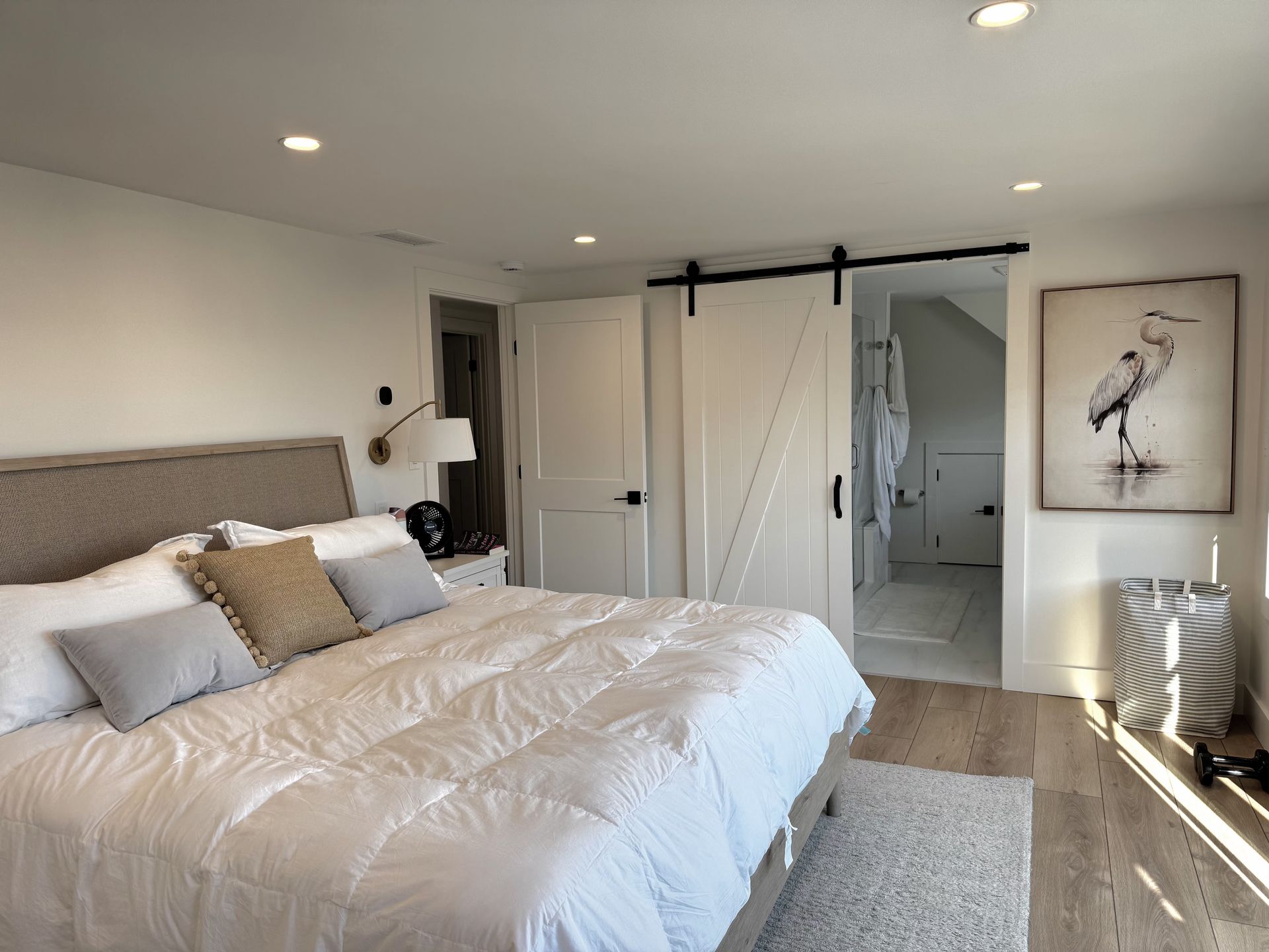 Bright modern bedroom with a white bed, sliding barn doors, and a framed bird print.