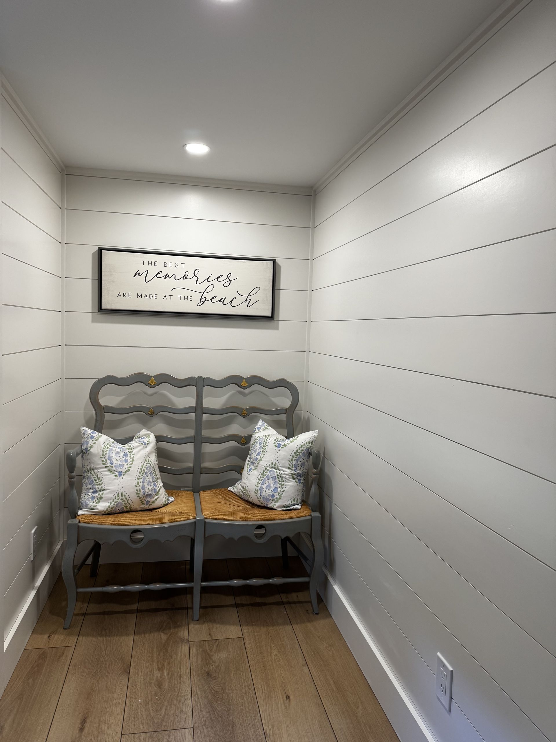 Small white entry nook with bench seating, patterned pillows, wood floor, and framed wall art.