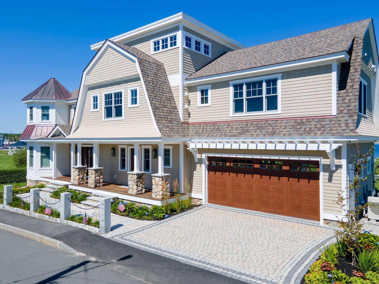 Modern coastal-style house exterior with stone siding, white trim, and a double garage on a sunny day