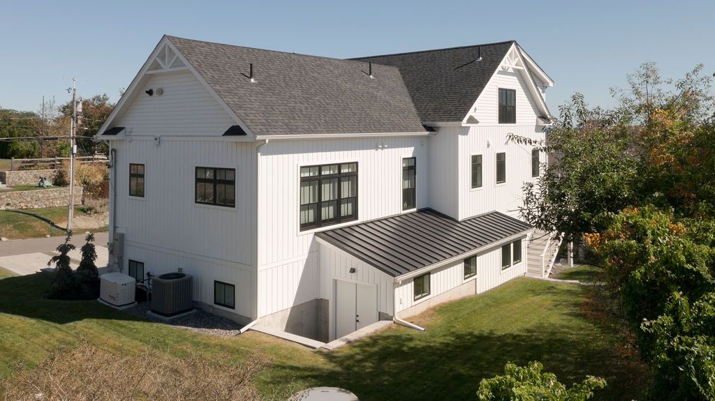 White two-story house with gray roof, large windows, and a covered porch in a grassy yard.