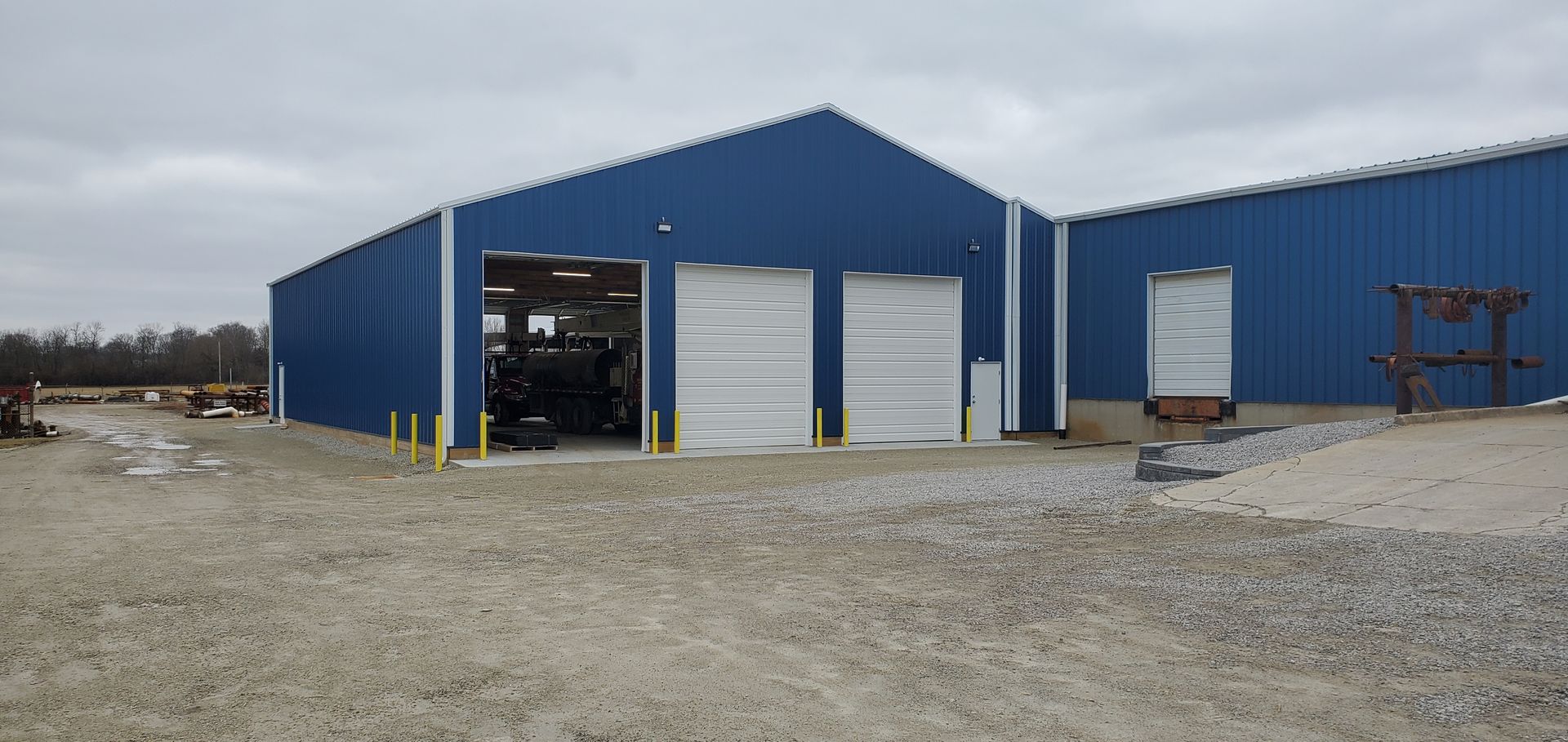 Blue metal industrial building with three garage doors on a gravel lot.