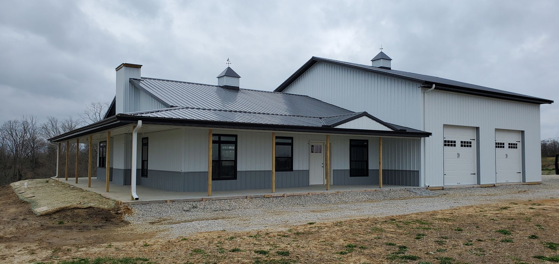 White barn with a porch and garage doors under a cloudy sky.