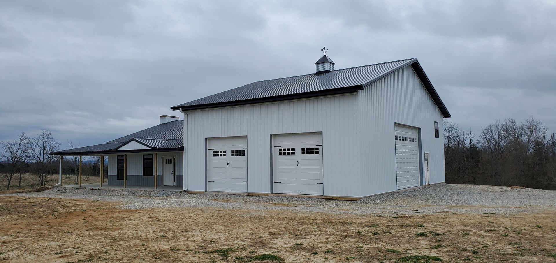White building with garage doors and a covered porch under an overcast sky.
