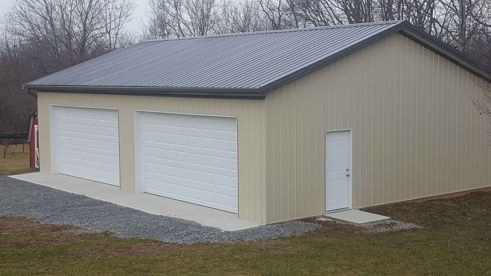 Tan metal garage with two garage doors and a small entry door. Gray roof. Outdoors.