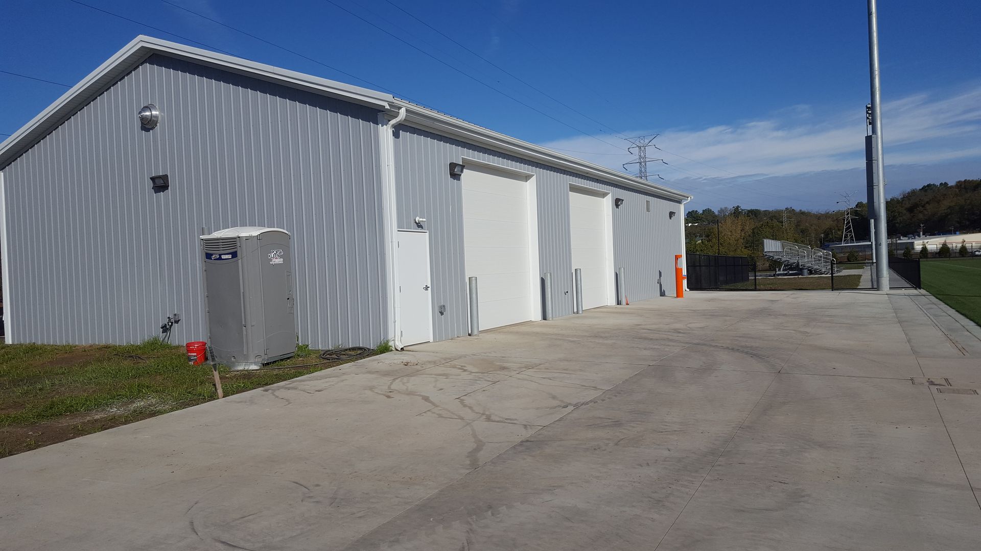 Gray metal building with three white garage doors and a concrete driveway on a sunny day.
