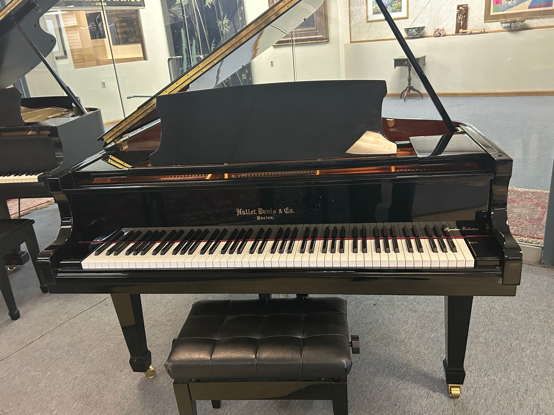 A glossy black grand piano with its lid open, positioned in a room with a matching leather bench.
