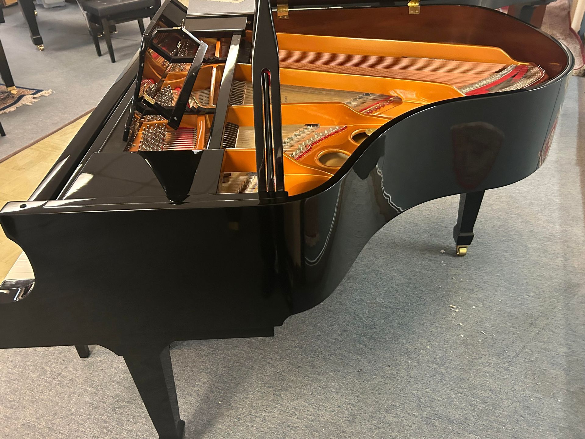 A high-angle view of a shiny black grand piano with its lid open, revealing the internal gold-colored frame and strings.