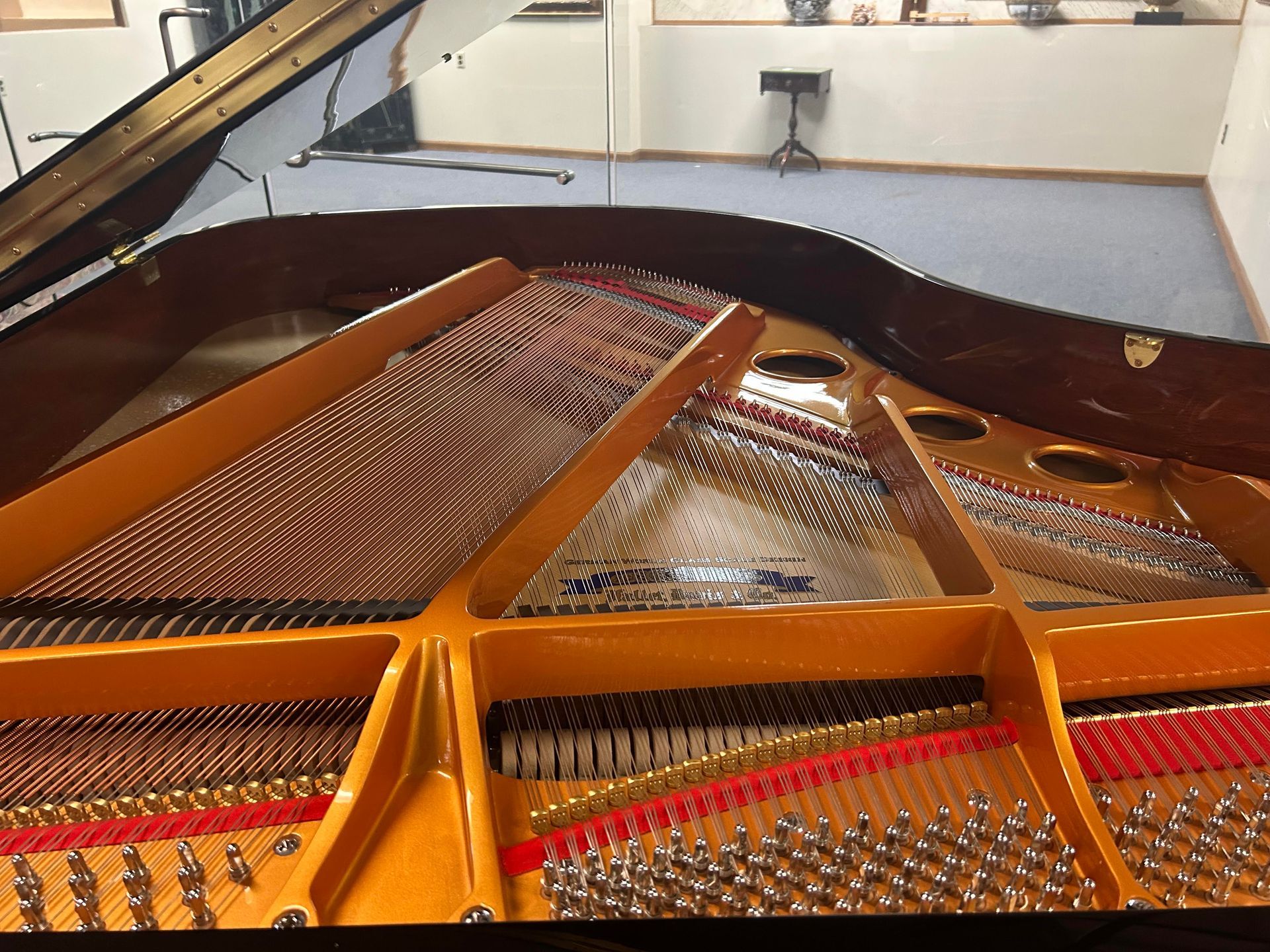 The interior of a grand piano, showing the golden harp, metallic tuning pins, and taut strings inside the wooden frame.