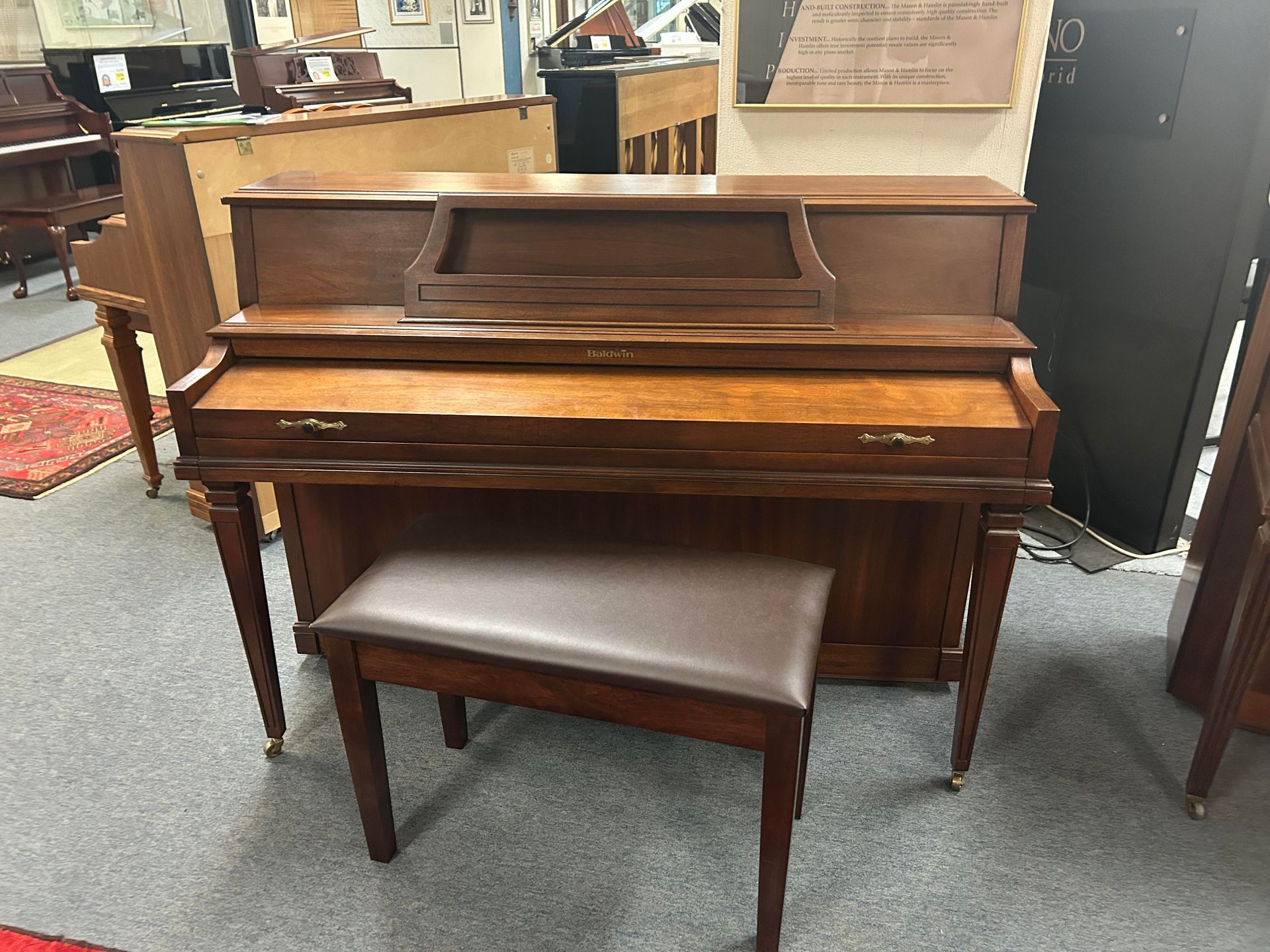 A piano with a bench is sitting in a room with other pianos.
