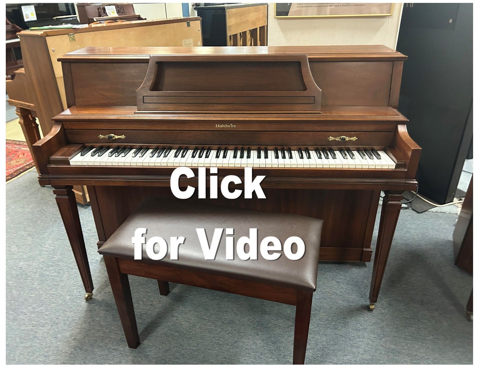 A piano with a bench and the words click for video below it