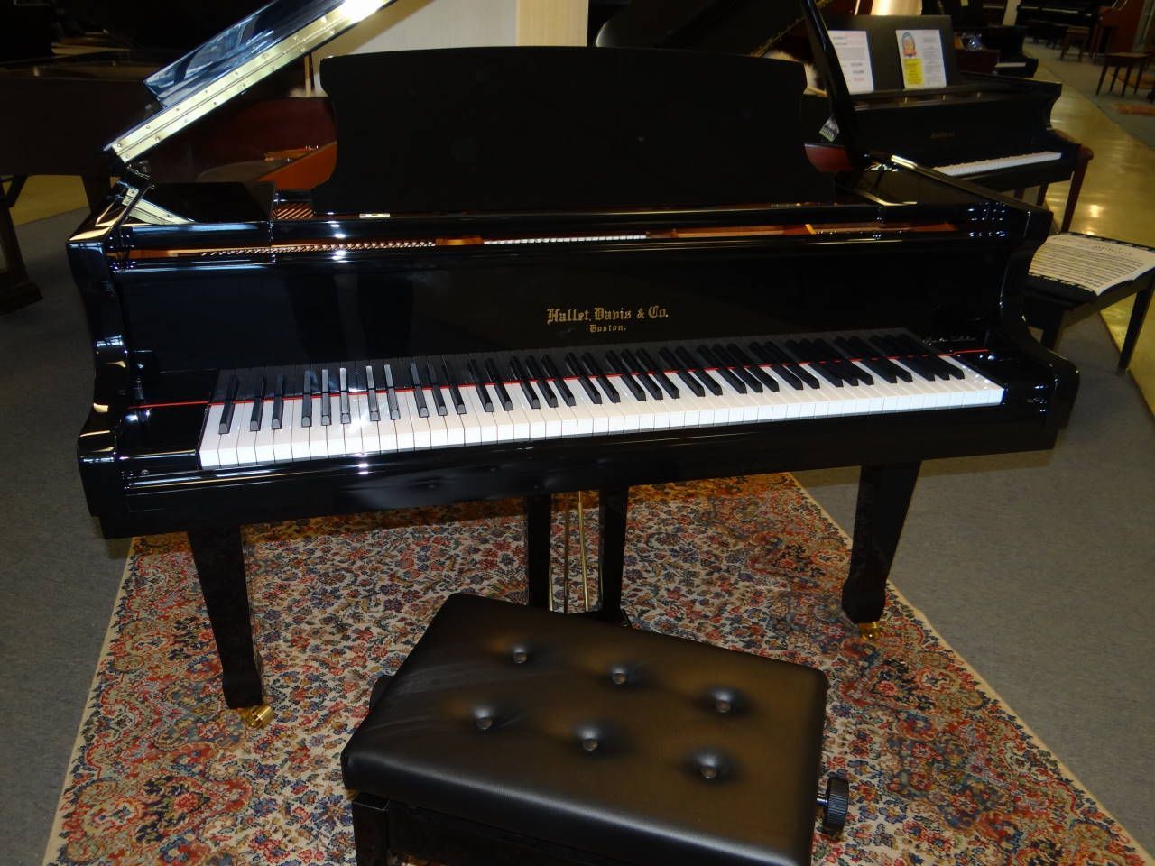 A black grand piano sits on a rug next to a black stool