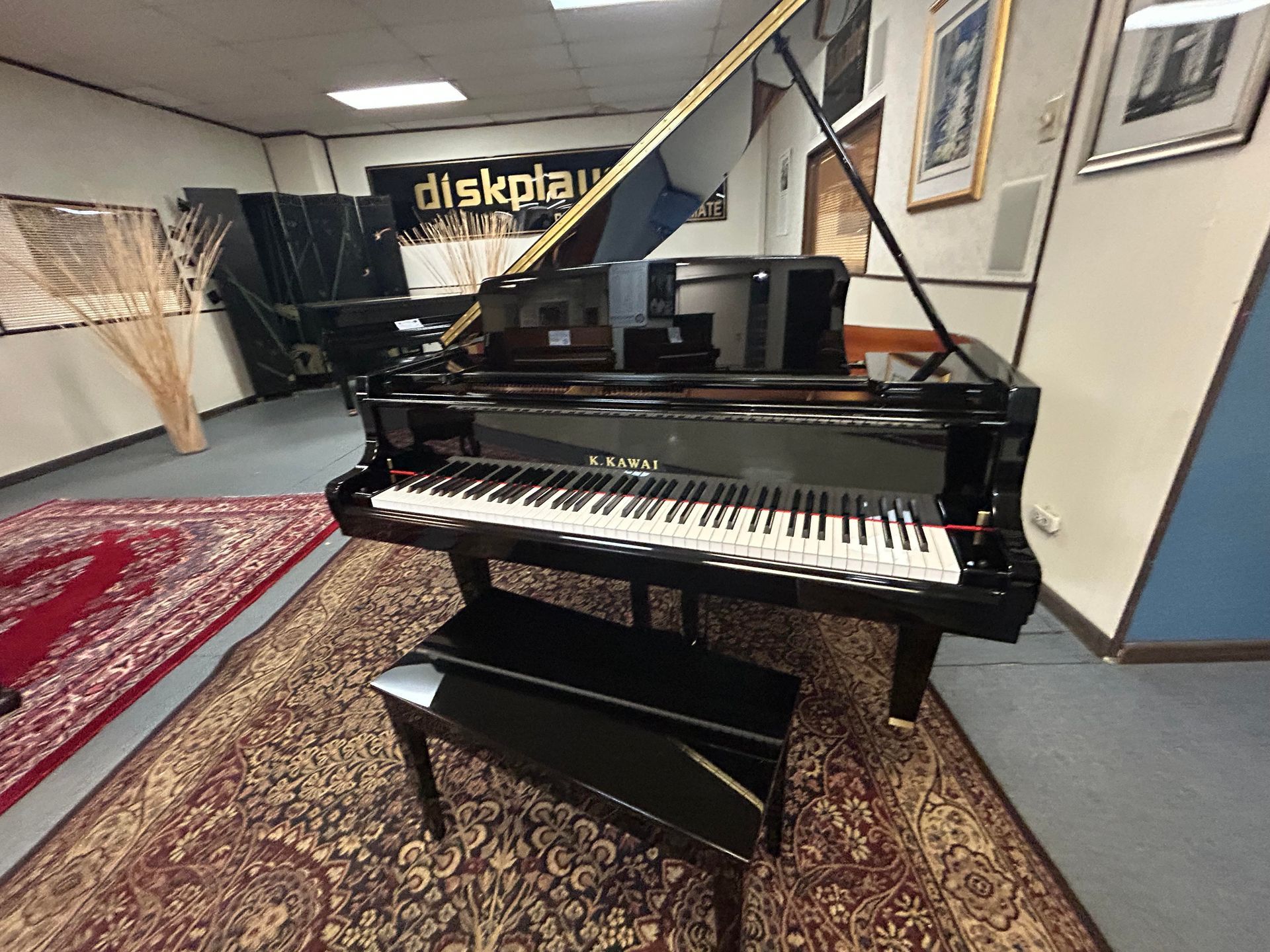 A shiny black grand piano with bench sits on a patterned rug, in a showroom.