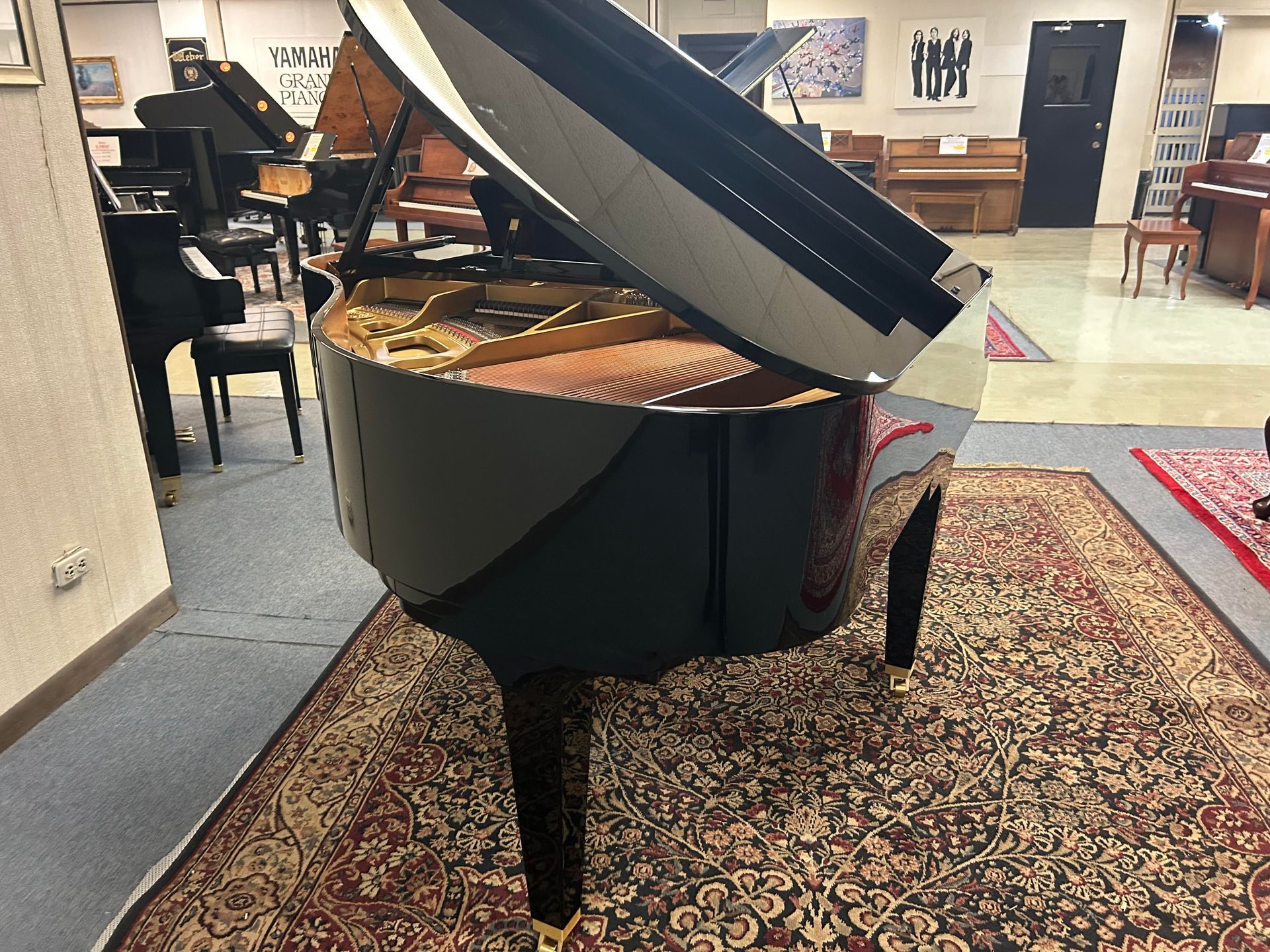 Grand piano with lid open, in a showroom, on a patterned rug.