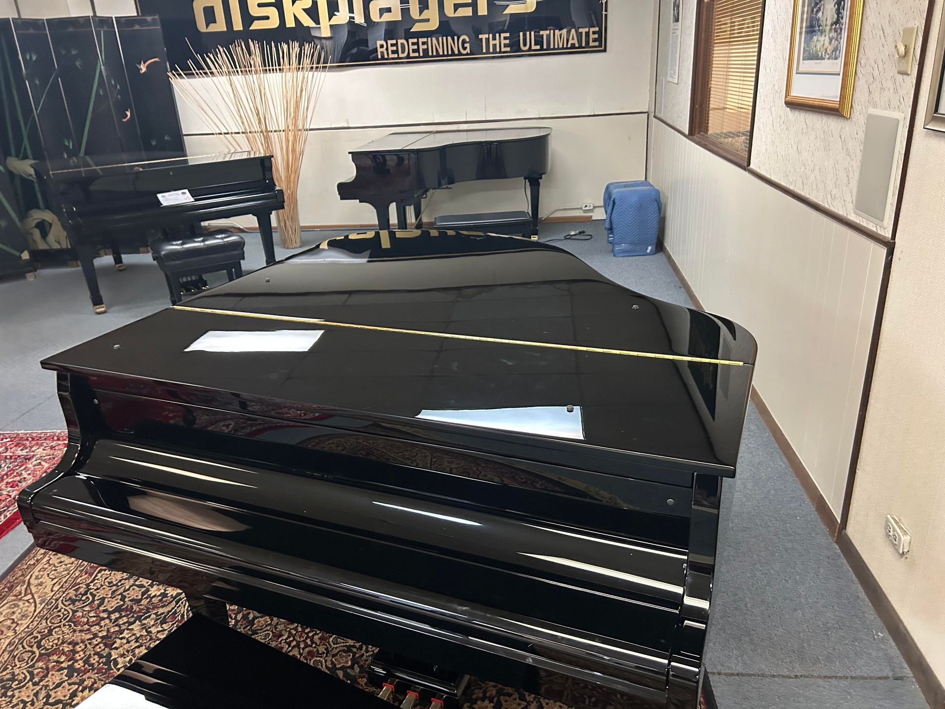 Black grand piano in a showroom, with other pianos and decor in the background.