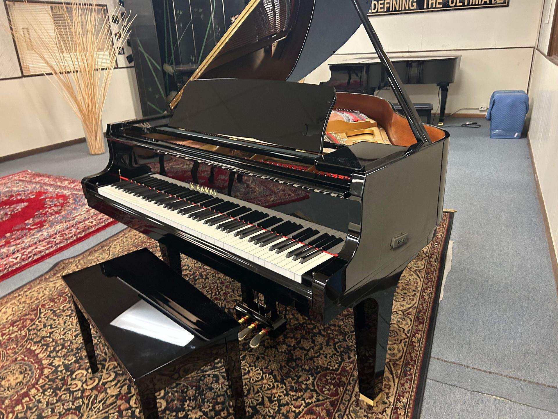Grand piano with open lid, black glossy finish, on ornate rug, with matching bench.