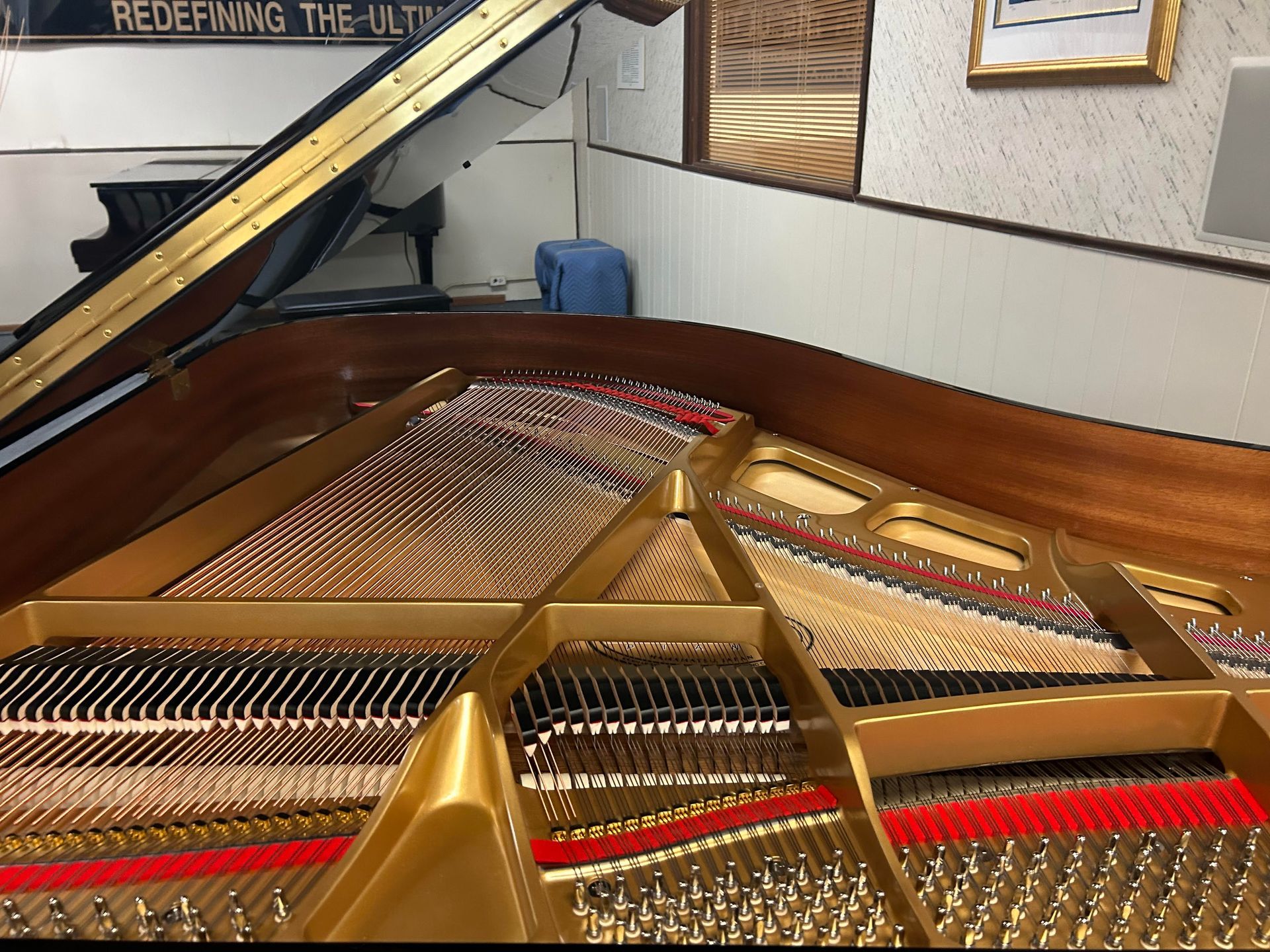 Open grand piano interior showing strings, hammers, and wood frame. Gold accents and red felt visible.