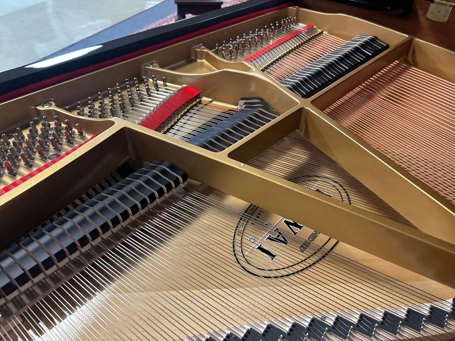 Inside view of a Kawai grand piano with strings and soundboard visible; gold, black, and red colors.