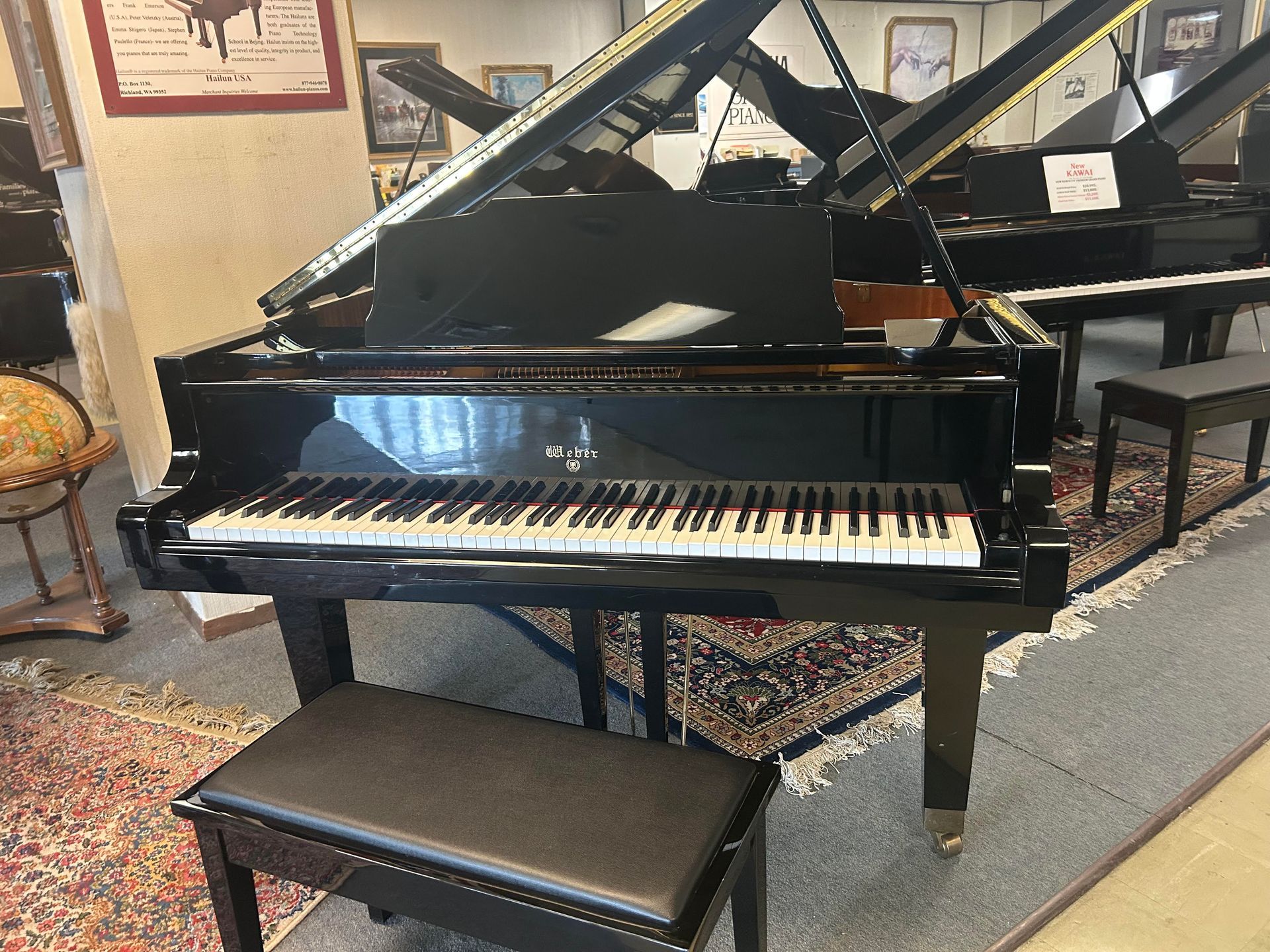 Black grand piano with open lid, set in a showroom with a black bench in front.