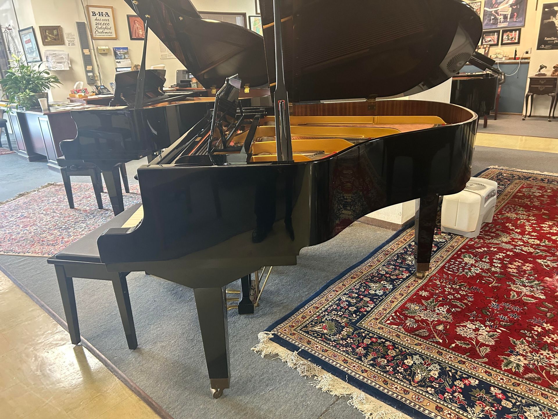 A grand piano with open lid on a patterned rug; another piano in the background.