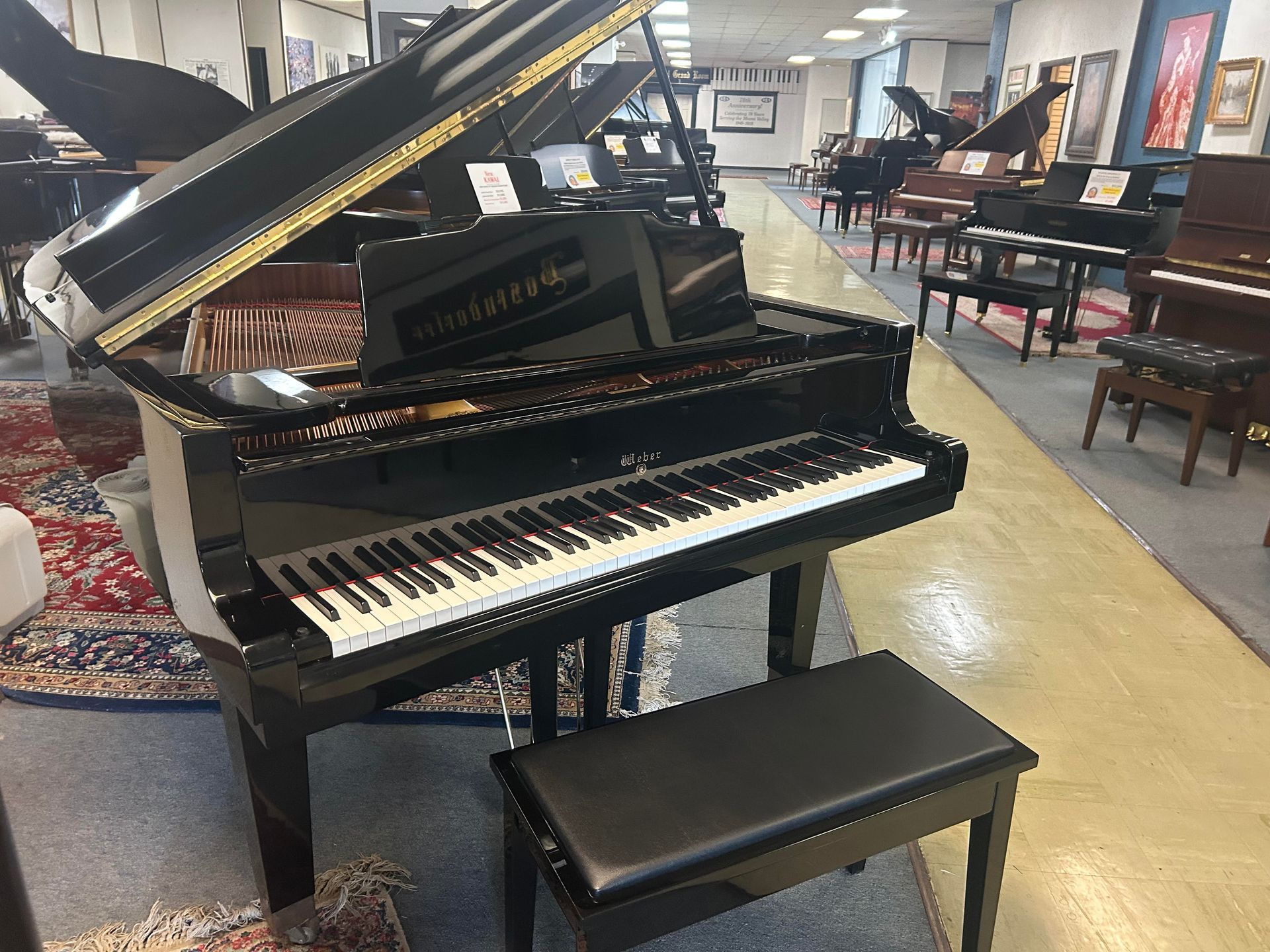 Black grand piano with open lid, in a piano showroom. Includes piano bench.