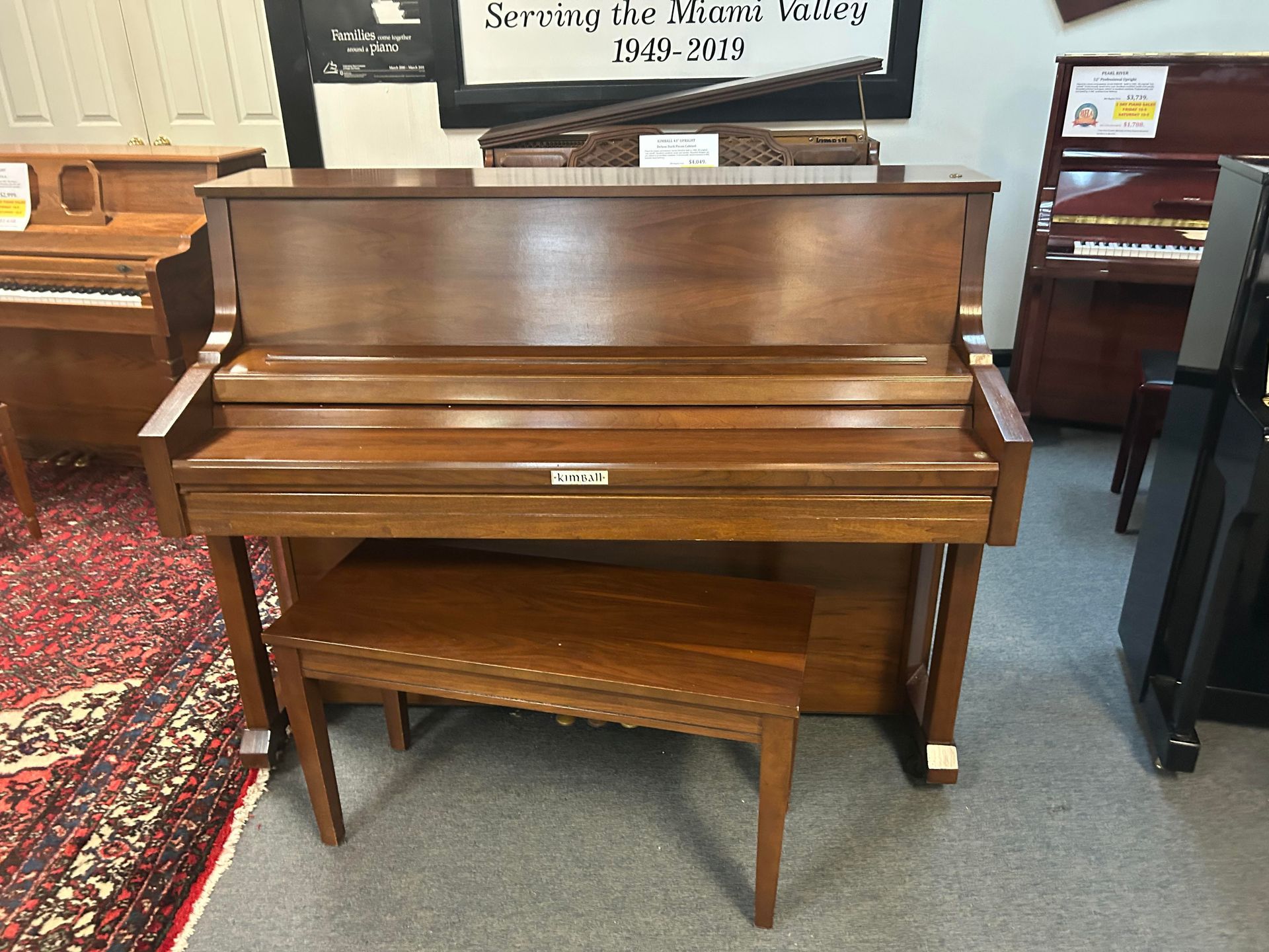 A closed brown Kimball Upright piano with a bench
