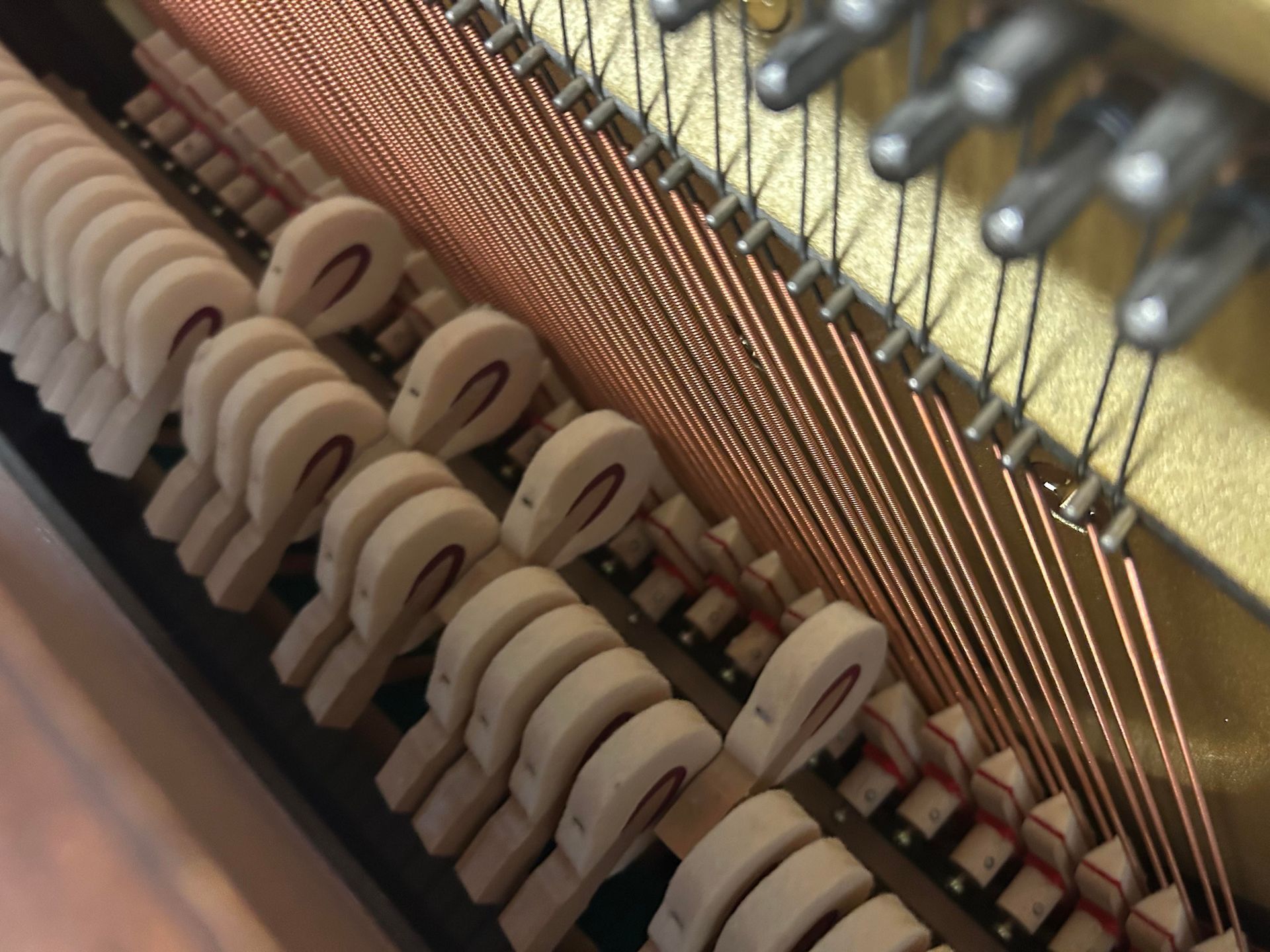 Interior view of a piano showing hammers striking copper strings. Close-up with visible wood, metal, and felt.