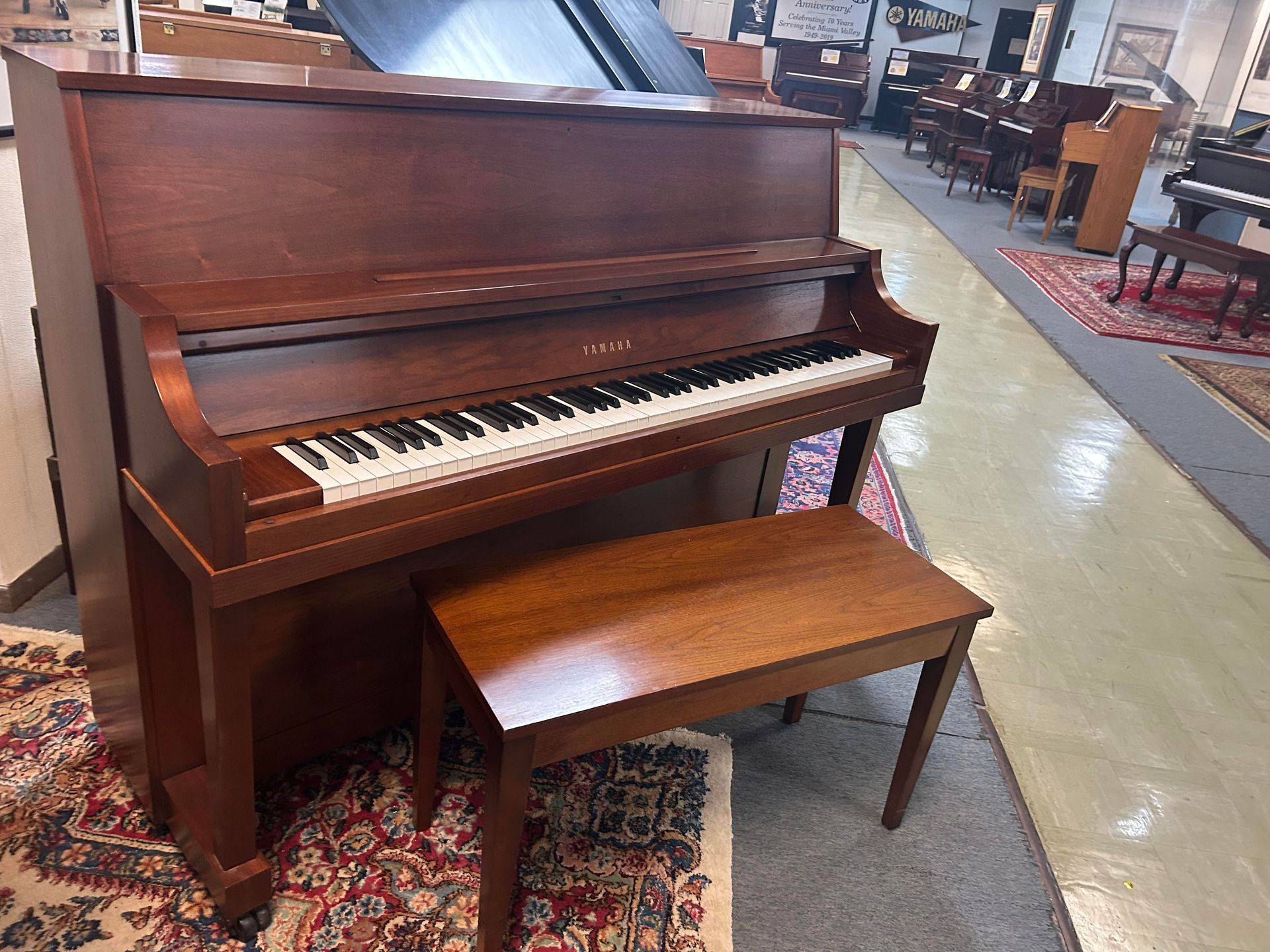 A wooden upright piano with a matching bench in a showroom.